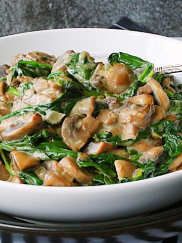 Creamy Mushrooms and Spinach in a white bowl with a serving spoon.