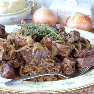 A platter filled with French Onion Short Ribs with fresh thyme sprigs on top and a bowl of mashed potatoes in the background.