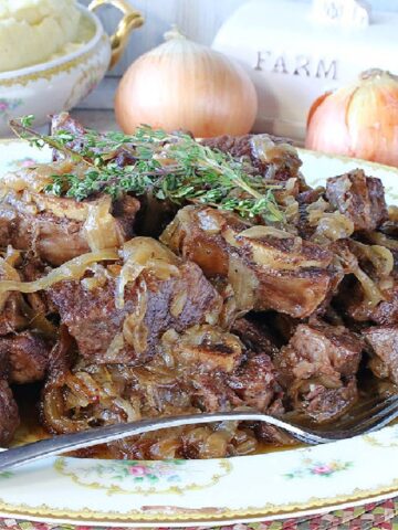 A platter filled with French Onion Short Ribs with fresh thyme sprigs on top and a bowl of mashed potatoes in the background.