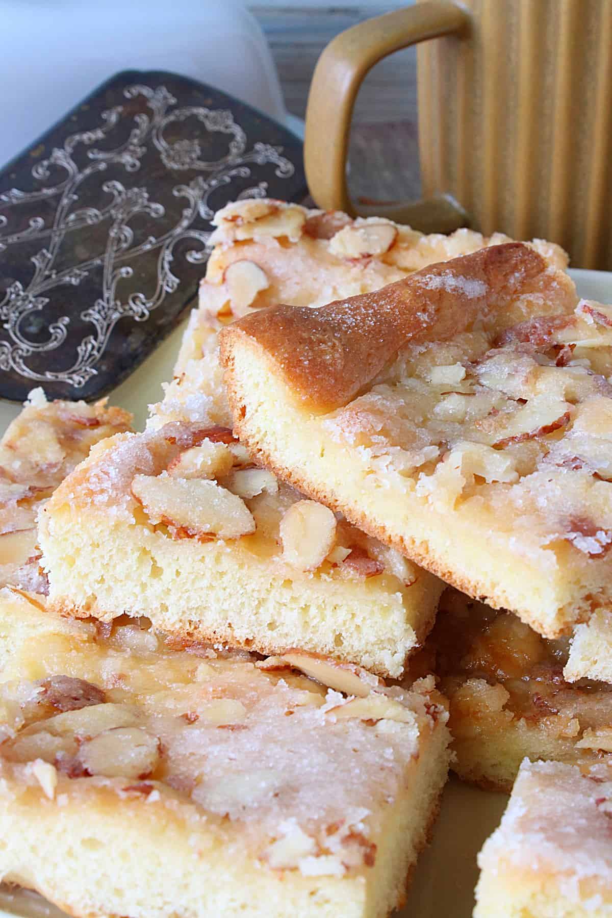 A stack of German Zuckerkuchen on a platter with a spatula and coffee cup in the background.