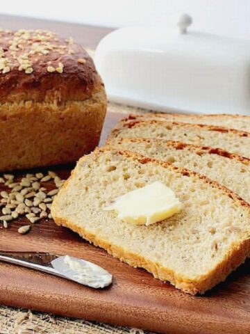 Three slices of Oatmeal Honey Bread on a cutting board with some butter.