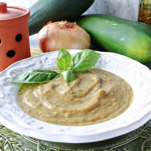 A white bowl filled with Roasted Garlic and Zucchini Soup along with a sprig of basil.