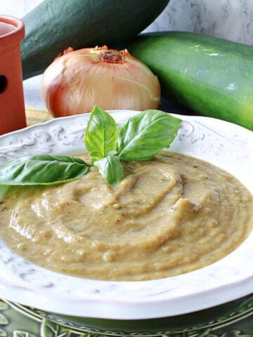 A white bowl filled with Roasted Garlic and Zucchini Soup along with a sprig of basil.