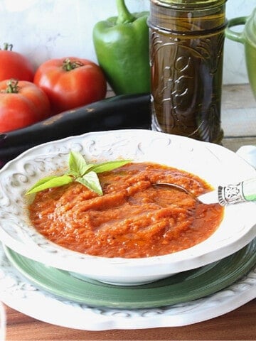 A serving of Roasted Tomato and Vegetable Soup in a bowl with fresh veggies in the background.