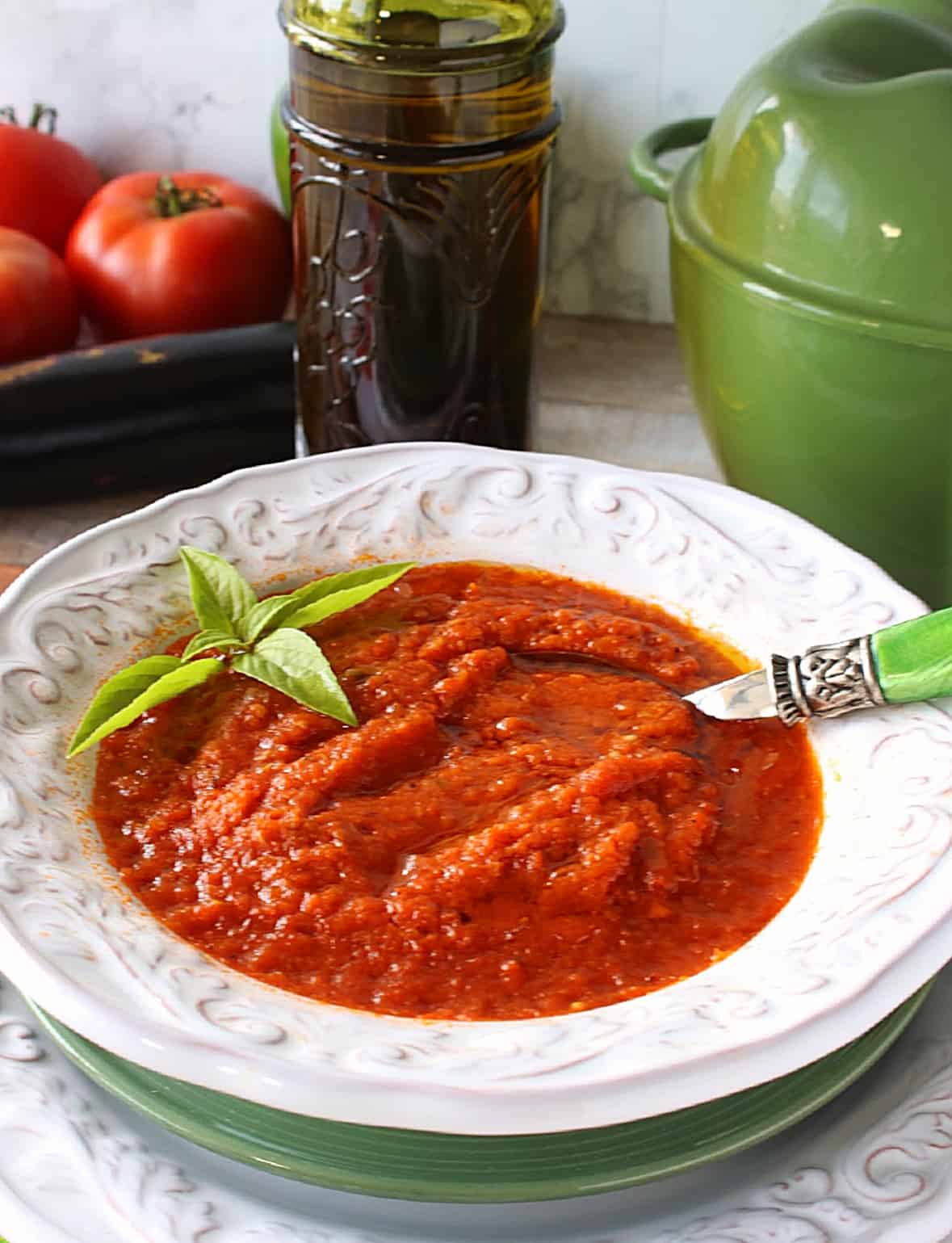 A white bowl filled with red Roasted Tomato and Vegetable Soup along with some basil leaves on top.