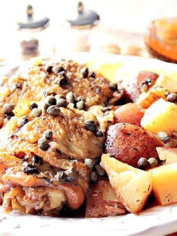 A serving of Slow Cooker Chicken Vesuvio on a plate with capers, potatoes, and chicken.