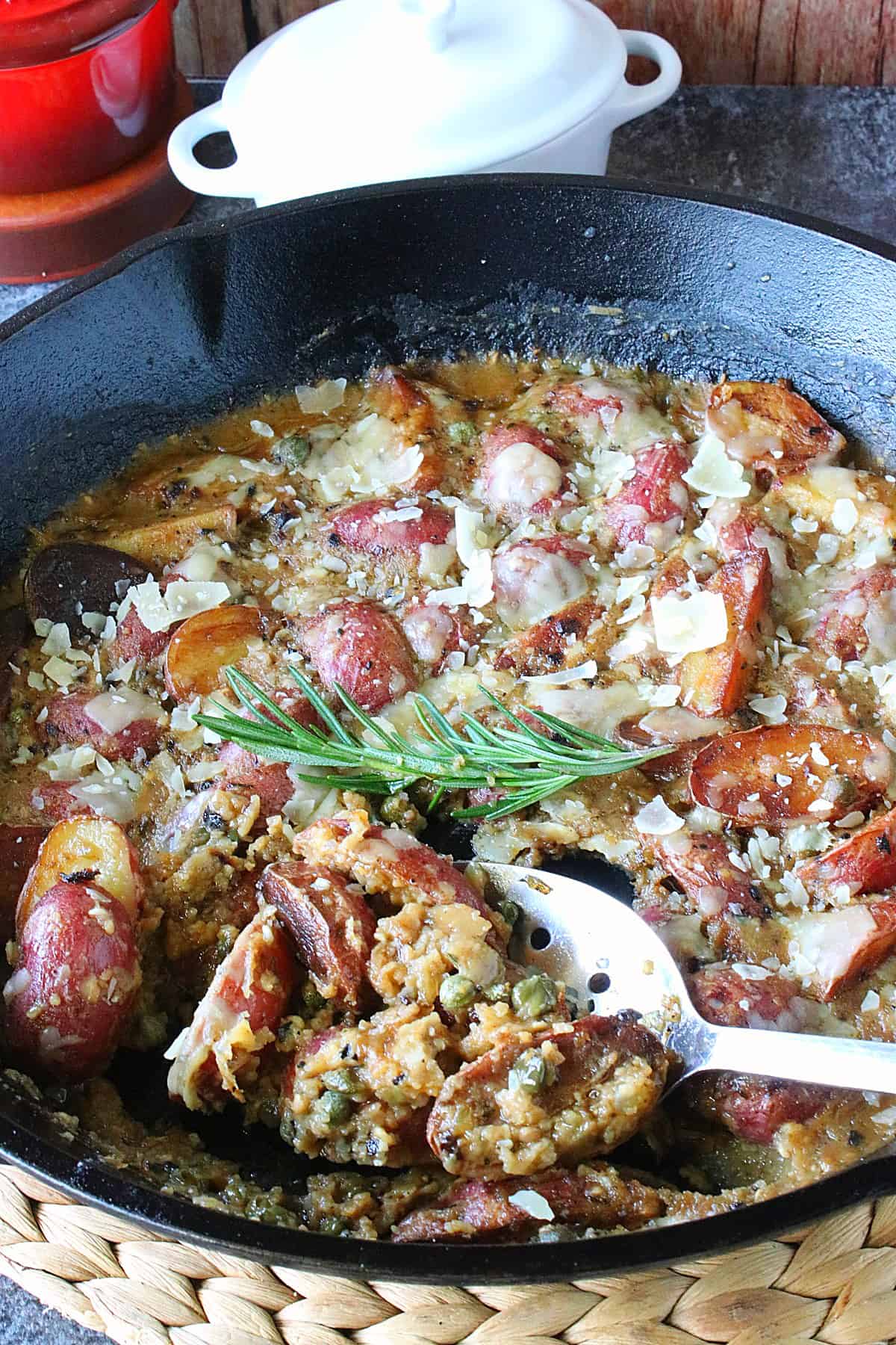 A black cast iron skillet filled with red Vesuvio Potatoes and Gravy along with a green sprig of rosemary.