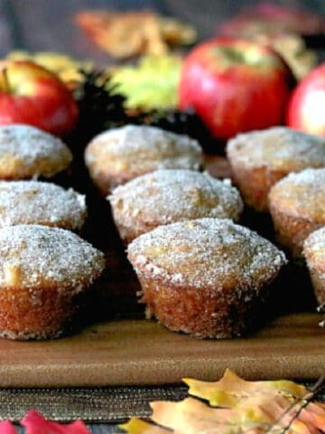 Cinnamon and Sugar Apple Cider Donut Muffins on a wooden board with apples in the background.