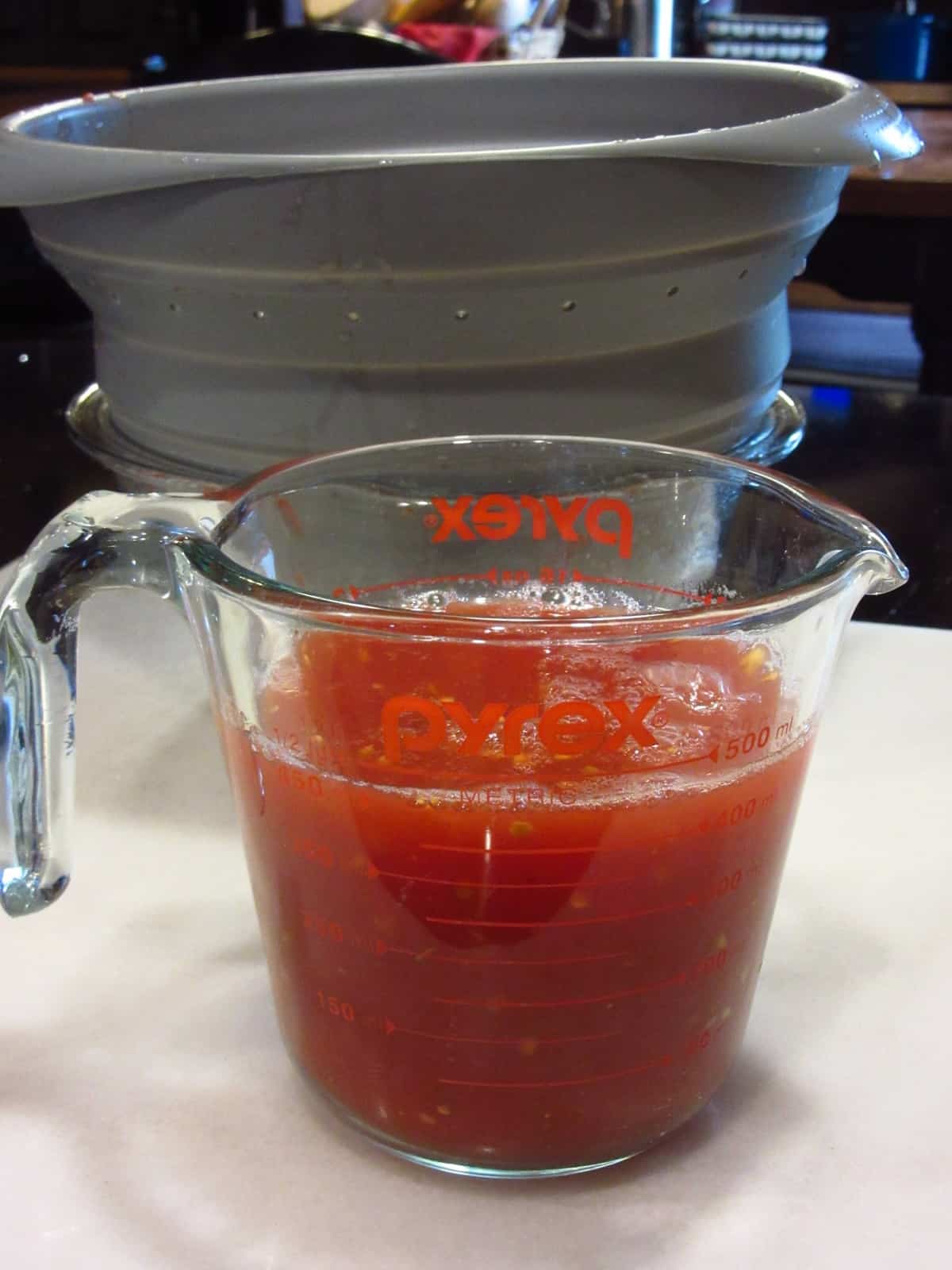 A glass measuring cup with tomato water. 