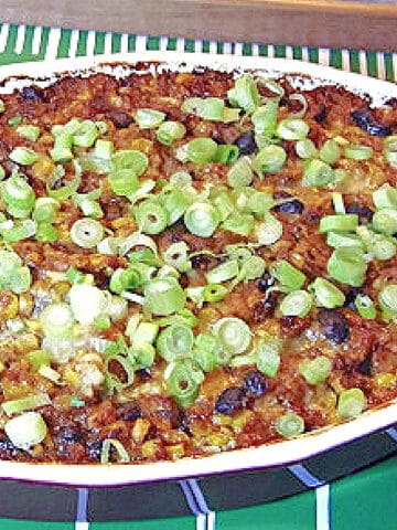 Cheesy Corn and Black Bean Dip in a casserole dish topped with scallions.