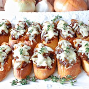 French Onion Crostini with melted cheese and fresh thyme on a plate.