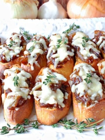 French Onion Crostini with melted cheese and fresh thyme on a plate.