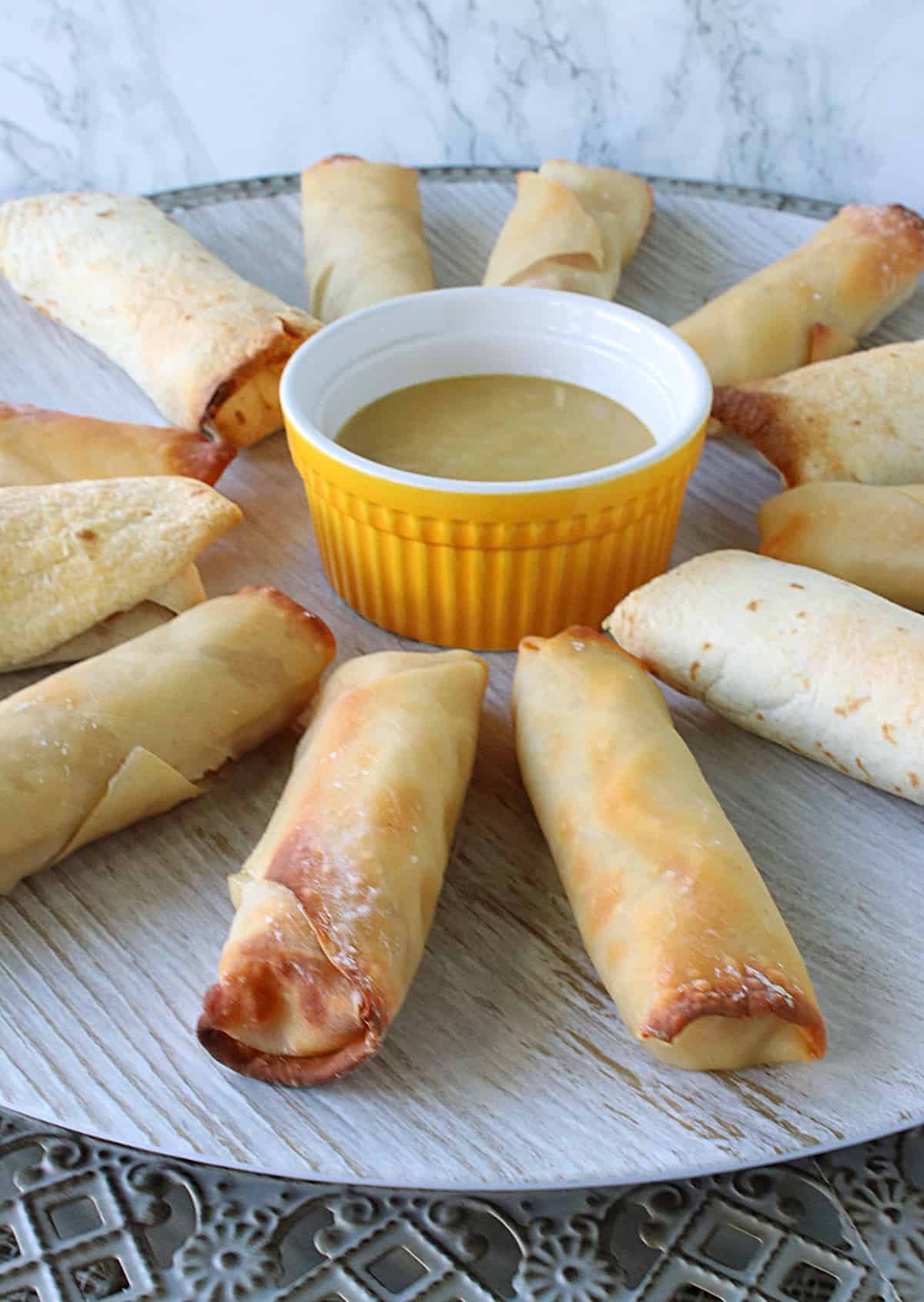 A round platter with Ham and Cheese Eggrolls and some dipping sauce in the middle.