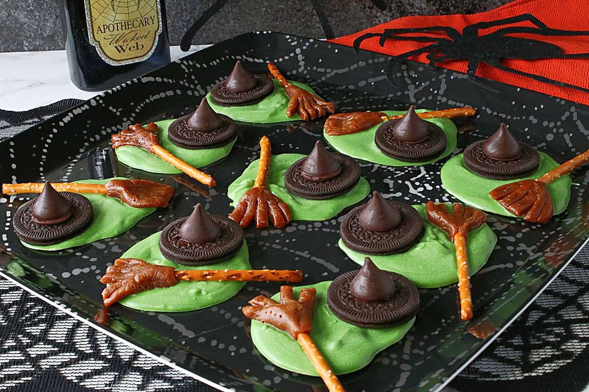 A square black plate filled with fun, green Melted Witch Candy with broomsticks and hats.