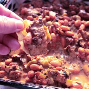 A hand with a chip loaded with Cheesy Sausage Bean Dip.