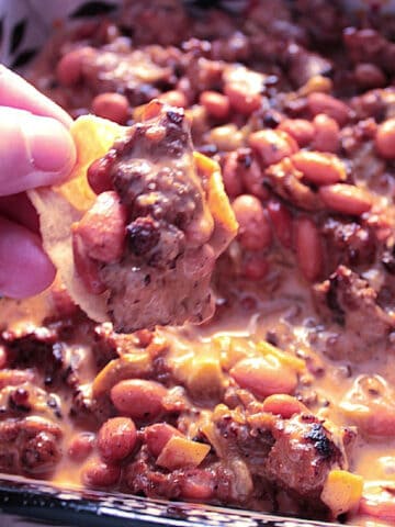 A hand with a chip loaded with Cheesy Sausage Bean Dip.