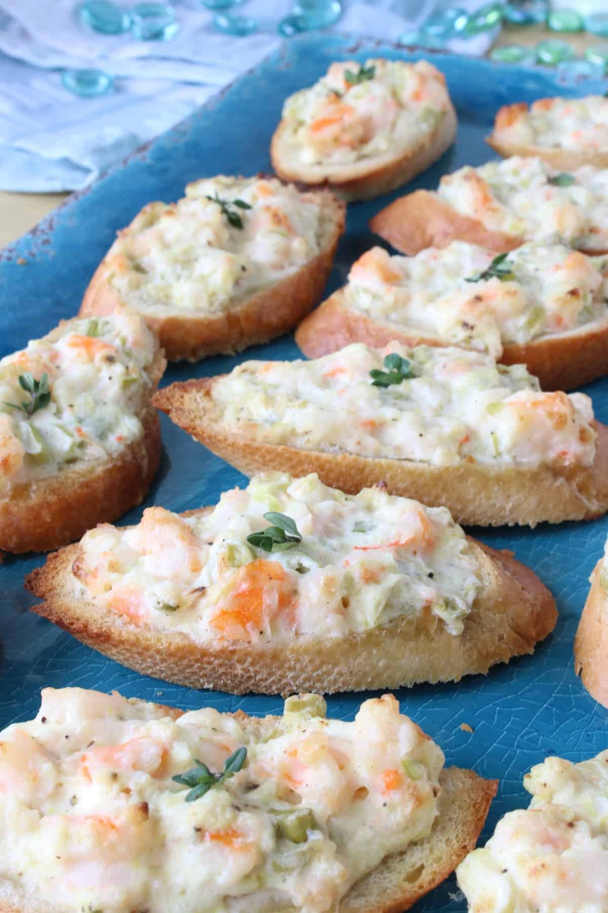 A blue platter filled with Shrimp Rangoon Garlic Toasts with a thyme leave on top.