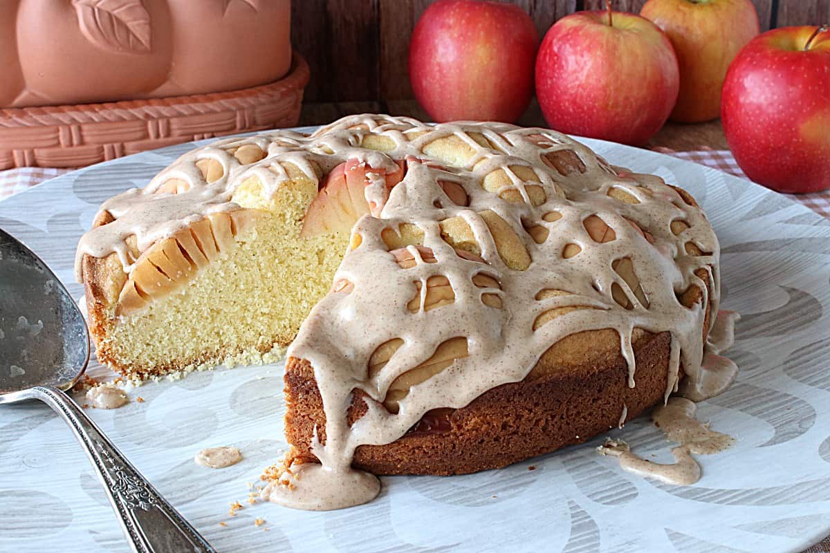 A German Sunken Apple Cake with a glaze on a platter with a slice taken out.