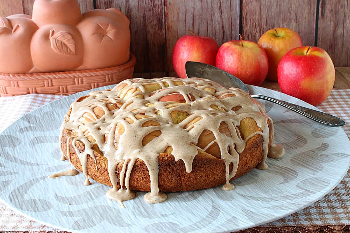 A glazed German Sunken Apple Cake on a round platter with a cake server.