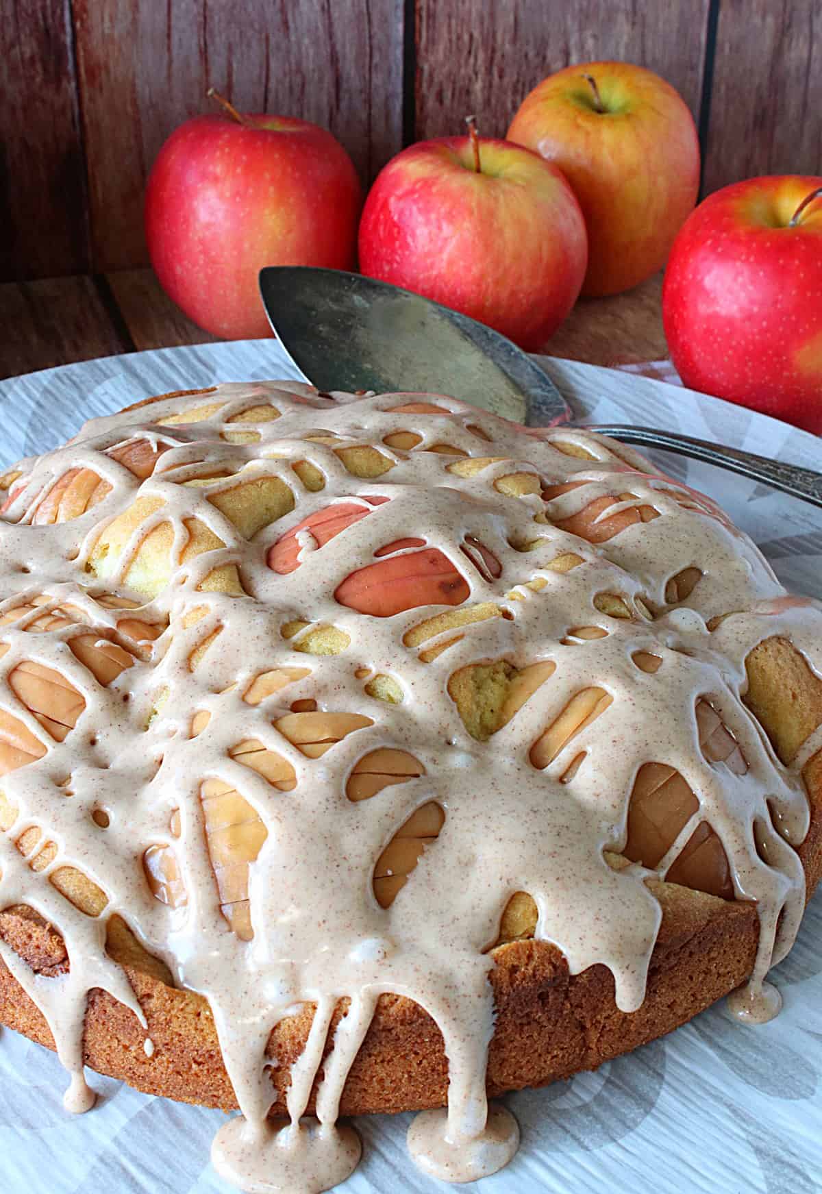 A pretty glazed German Sunken Apple Cake on a platter with apples in the background.