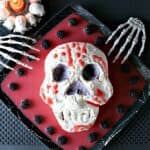 A spooky Swiss Meringue Skull on a platter with red blood and berries.