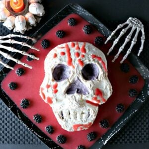 A spooky Swiss Meringue Skull on a platter with red blood and berries.