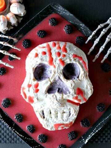 A spooky Swiss Meringue Skull on a platter with red blood and berries.