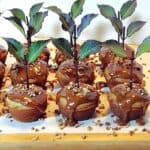 A wooden tray filled with Caramel Apple Cupcakes along with a stems, leaves, and chopped pecans.
