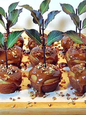 A wooden tray filled with Caramel Apple Cupcakes along with a stems, leaves, and chopped pecans.