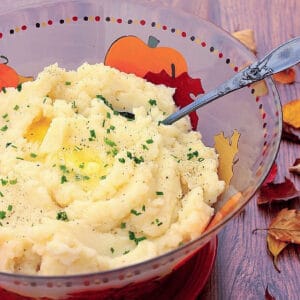 A serving bowl filled with Celery Root Mashed Potatoes with melted butter on top.