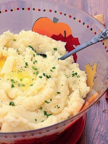 A serving bowl filled with Celery Root Mashed Potatoes with melted butter on top.