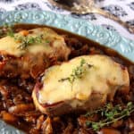 Two cheese covered French Onion Pork Chops on a blue platter.