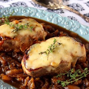 Two cheese covered French Onion Pork Chops on a blue platter.