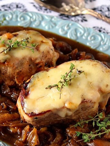 Two cheese covered French Onion Pork Chops on a blue platter.