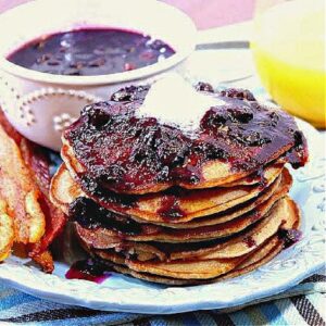 A stack of Whole Wheat Peanut Butter Pancakes topped with Blueberry Maple Syrup and butter on a plate.