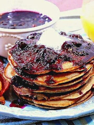 A stack of Whole Wheat Peanut Butter Pancakes topped with Blueberry Maple Syrup and butter on a plate.