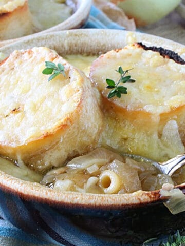 Two cheesy baguette slices on top of a bowl of French Onion Soup with Pasta.