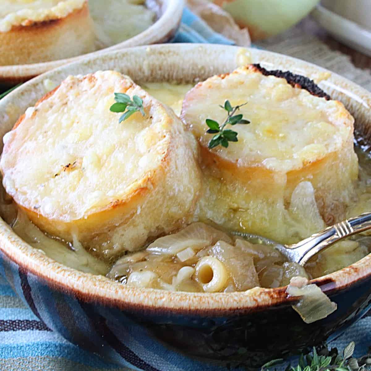 Two cheesy baguette slices on top of a bowl of French Onion Soup with Pasta.
