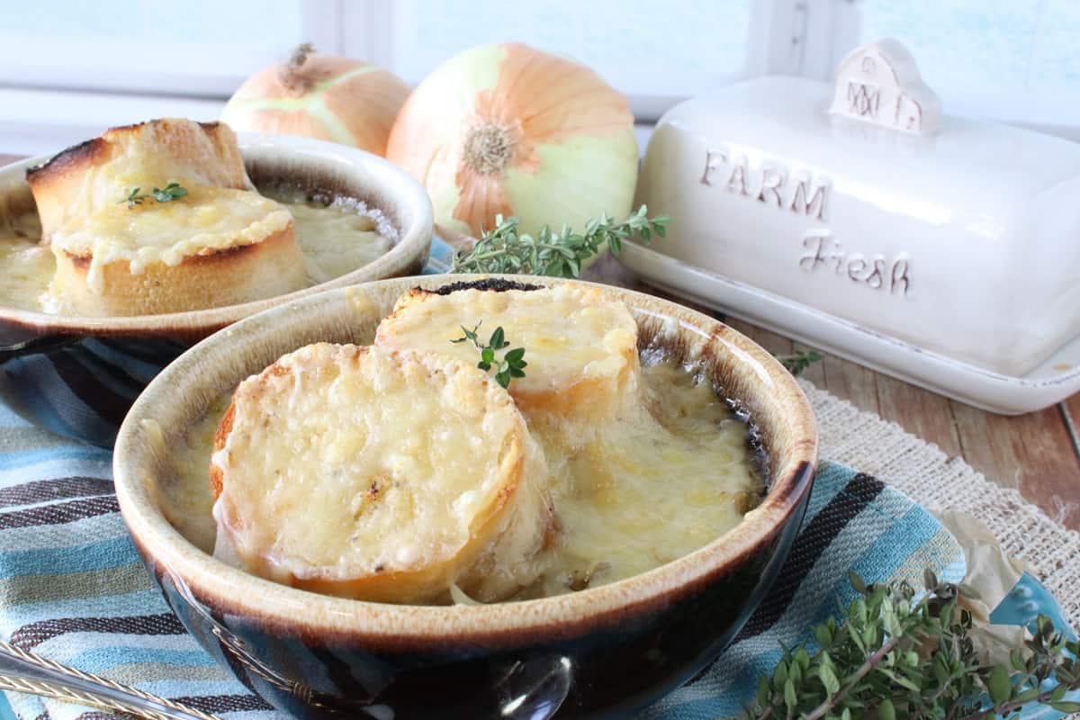 Two brown soup crocks filled with French Onion and Pasta Soup with melted cheese and thyme.