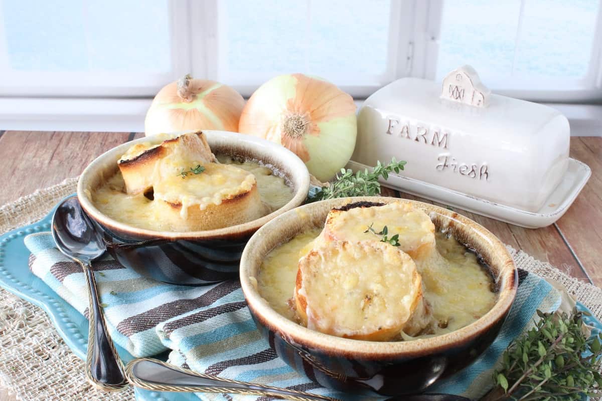 Two crocks of French Onion and Pasta Soup in a winter setting with spoons and napkins.