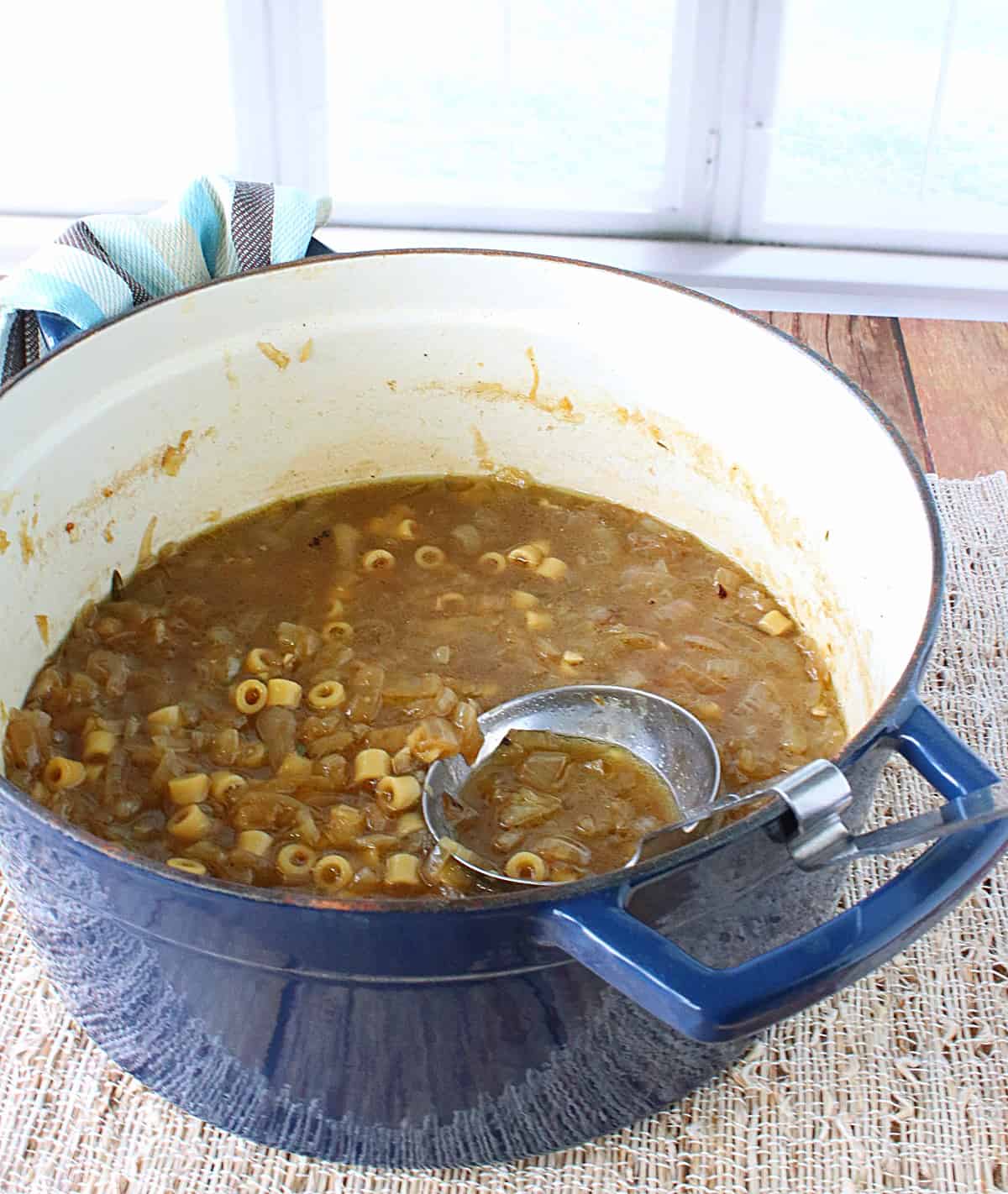 A blue Dutch oven filled with French Onion and Pasta Soup.