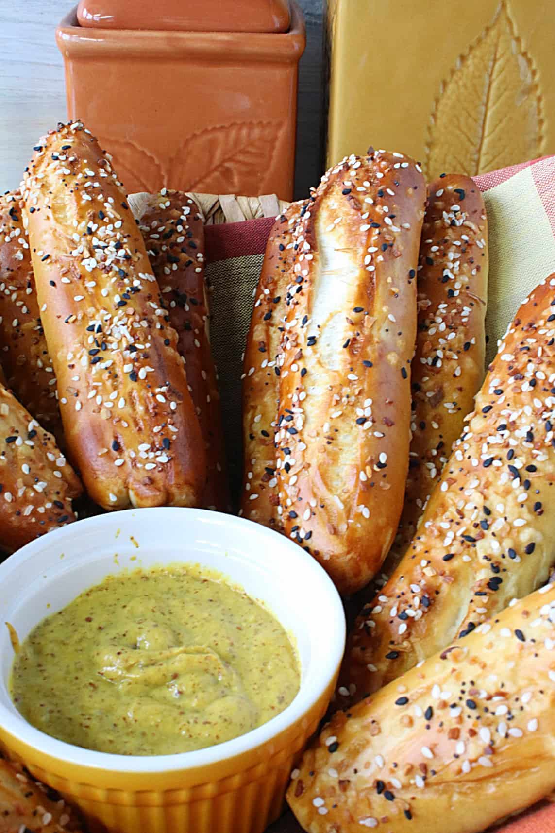 A bunch of golden brown Soft Pretzel Rods with everything seasoning in a basket with a mustard dipping sauce. 