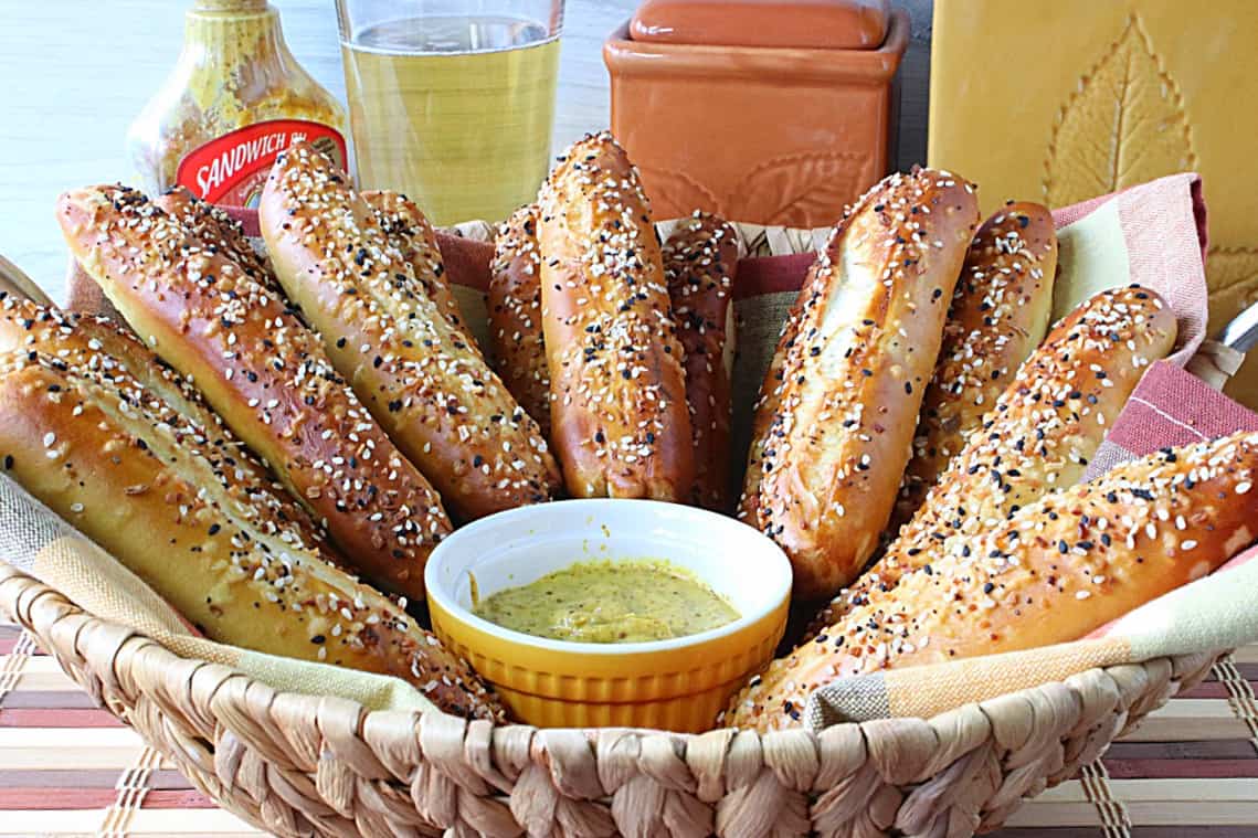 A splayed-out bunch of Soft Pretzel Rods in a basked with a small bowl of mustard in the center.
