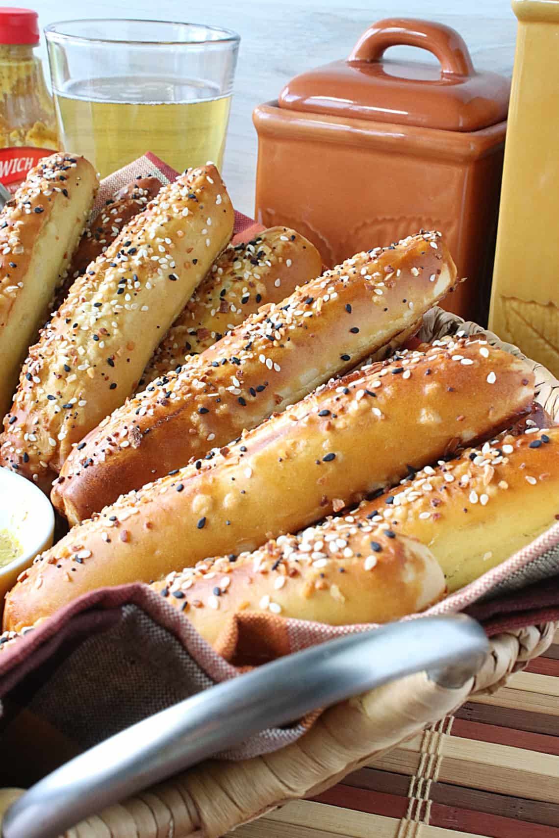 A bunch of golden-brown Soft Pretzel Rods in a basket with a glass of beer and some mustard in the background.