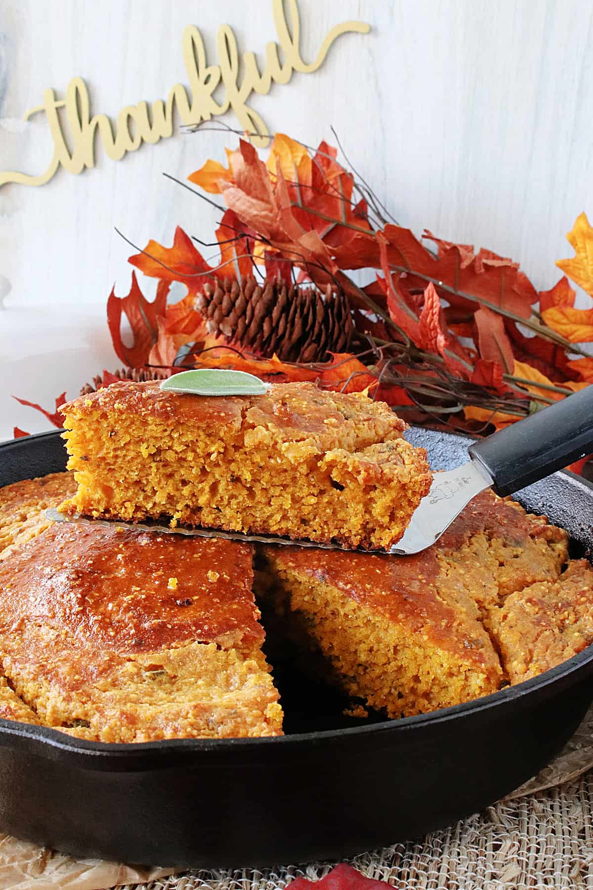 A cast iron skillet with baked Pumpkin Cornbread with Sage and fall leaves in the background.