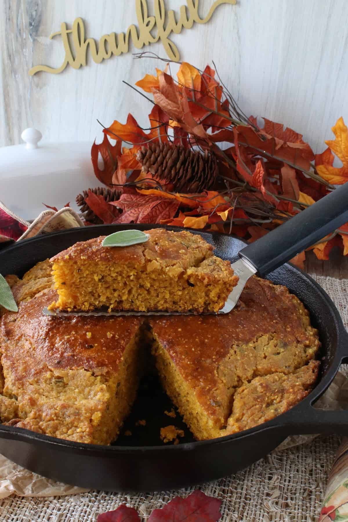 A black skillet filled with pumpkin sage cornbread with a slice taken out.