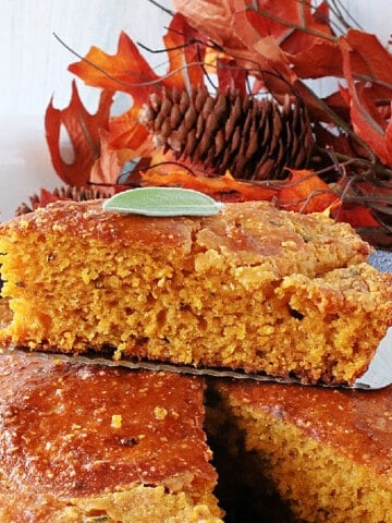 A triangle slice of Pumpkin Cornbread on a spatula with a sage leaf on top.