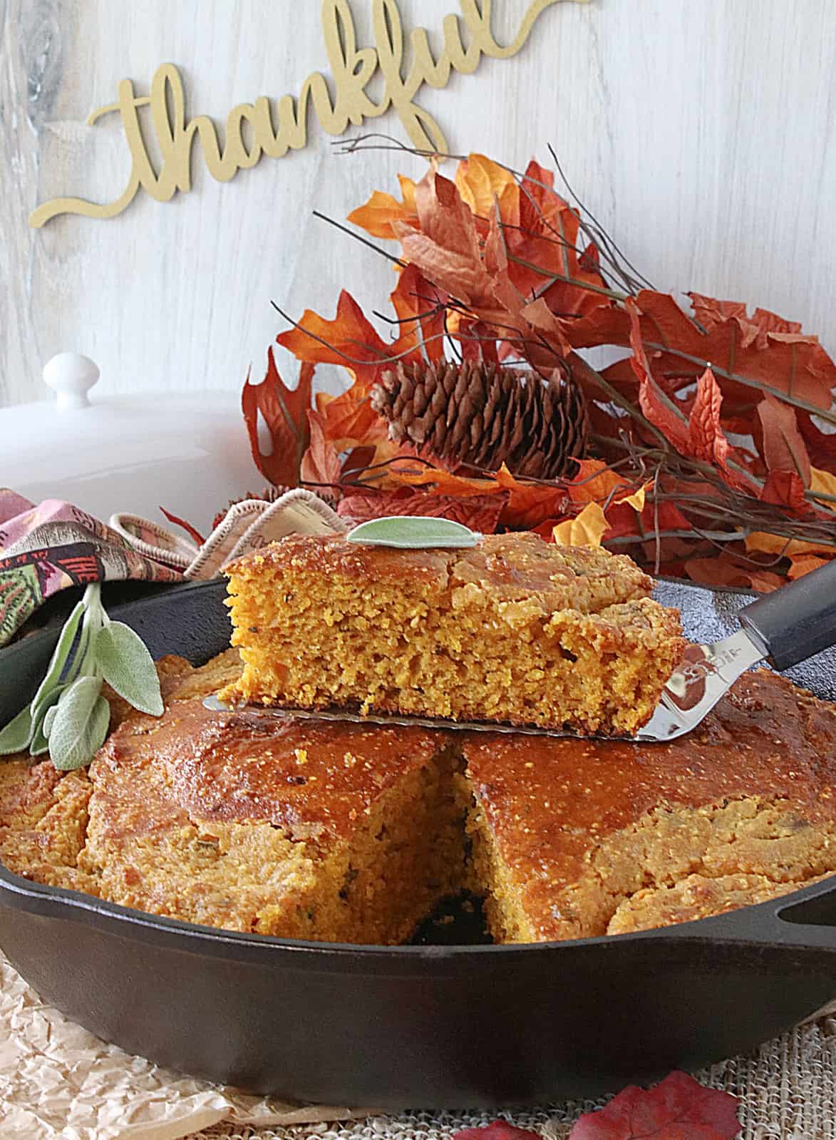Fall leaves in the background of a cast iron skillet filled with Pumpkin Cornbread with Sage. 