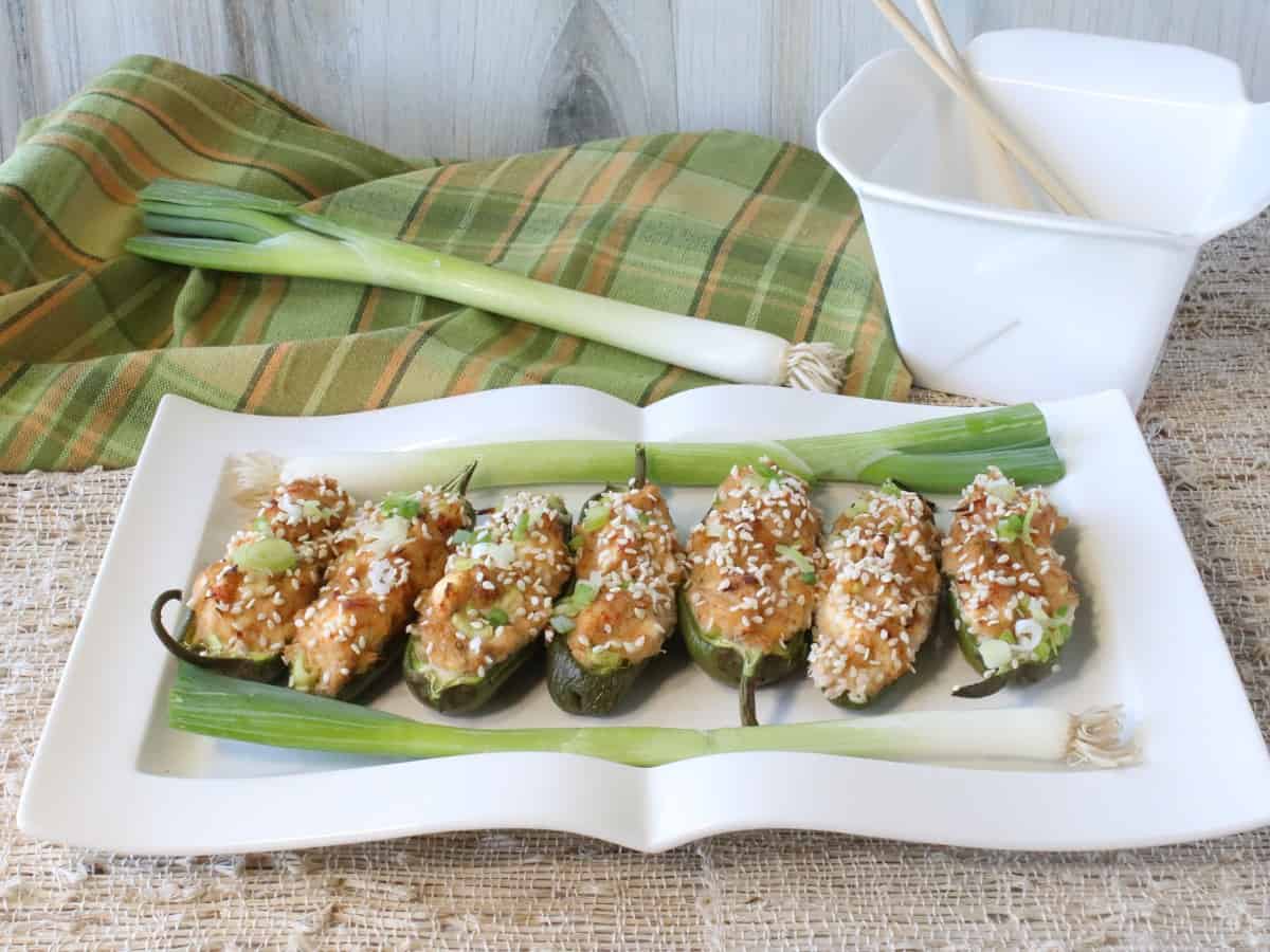 A white platter filled with Crab Rangoon Jalapeno Poppers along with scallions.