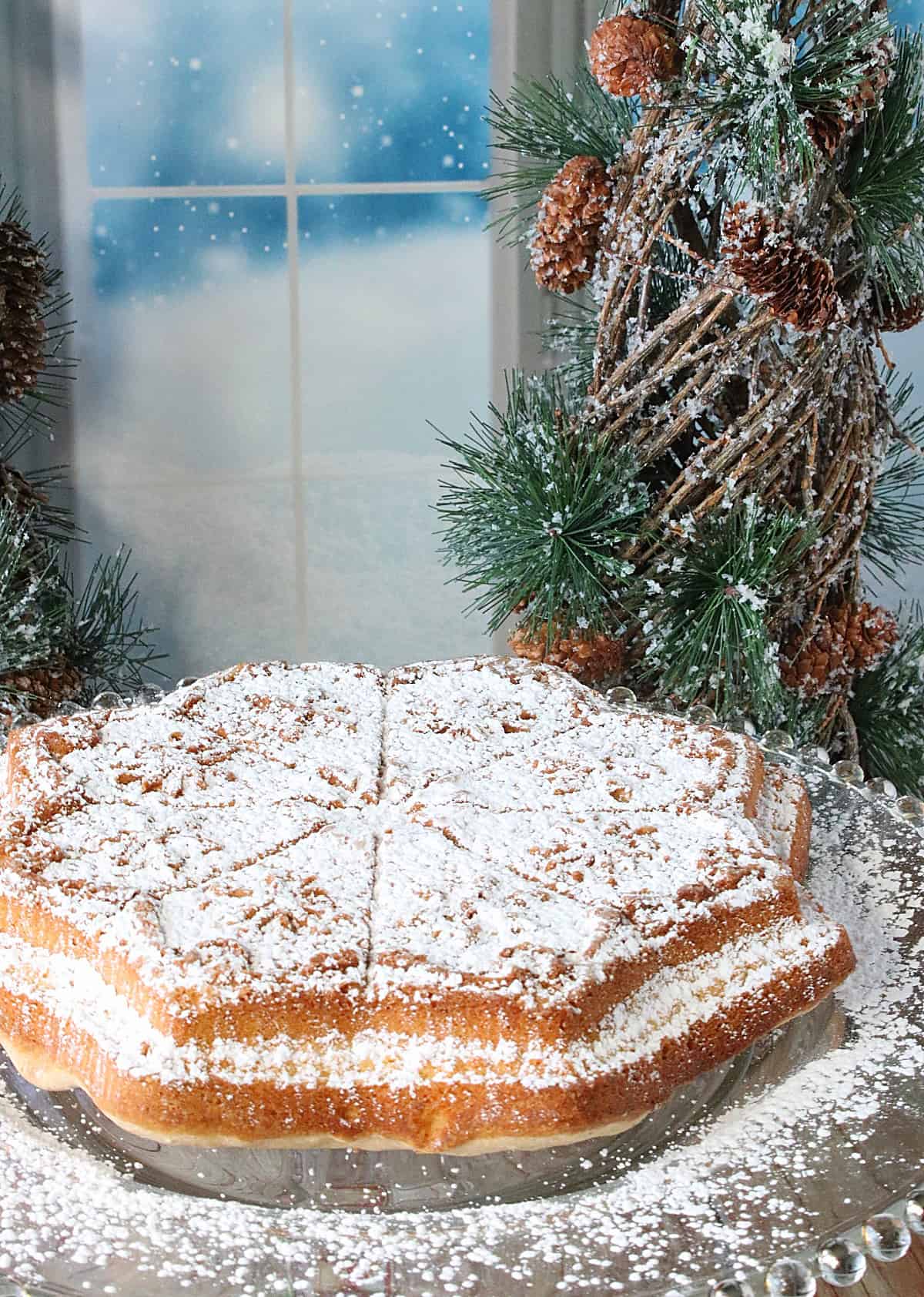 A snowflake-shaped Anise Cookie Bars Cookie on a plate in front of a snowy window scene. 